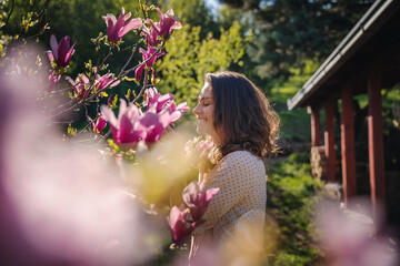 Young beautiful woman enjoying the spring of her home in the garden near a blooming magnolia tree inhaling the aroma of flowers