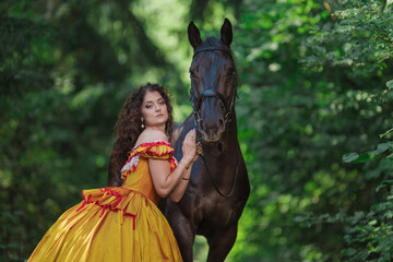 A young woman in a vintage yellow dress walks with a brown horse in a green park on a summer day