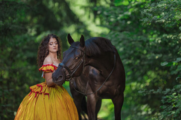 A young woman in a vintage yellow dress walks with a brown horse in a green park on a summer day