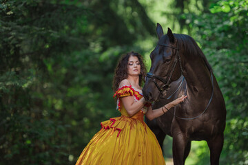 A young woman in a vintage yellow dress walks with a brown horse in a green park on a summer day