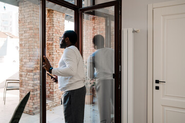 Black bearded man using mobile phone while standing in doorway
