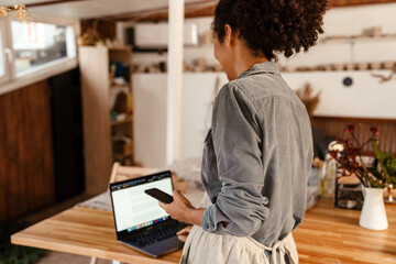 Young black ceramist woman using cellphone and laptop in her studio