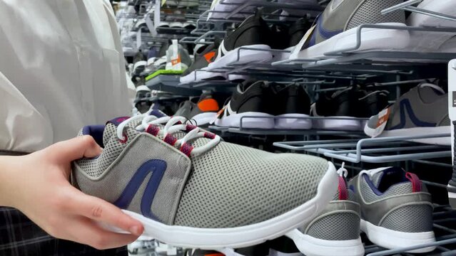 Someone chooses large-sized gray unisex sneakers at the sporting goods store