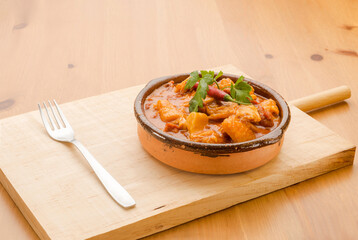 Typical Spanish food, stewed tripe a la madrilena. 
Horizontal view of food in a clay pot on a wooden table.
