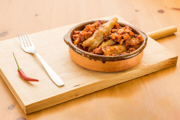 Typical Spanish food, lamb trotters with ham and chorizo. 
Horizontal view of food in a clay pot on a wooden table.