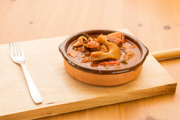 Typical Spanish food, pork nose in sauce. 
Horizontal view of food in a clay pot on a wooden table.