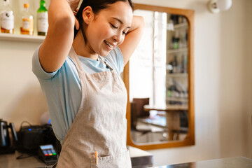 Young asian waitress wearing apron smiling while doing hairstyle