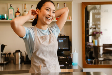 Young asian waitress wearing apron smiling while doing hairstyle