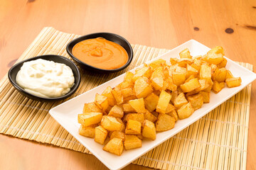 Typical Spanish food, potatoes with alioli sauce and brava sauce. Horizontal view of food on a white plate.
