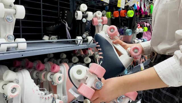Someone chooses retro style roller skates dark blue with pink wheels in the sports goods store 