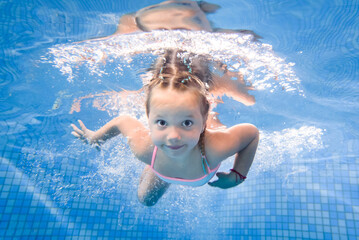 Little girl swims under water in paddling pool. Diving. Learning child to swim. Enjoy swimming and bubbles.