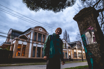 Happy young man with beard, knit wool hat and jacket, old stone column, old centuries building with...