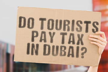 The question " Do tourists pay tax in Dubai? " is on a banner in men's hands with blurred background. Bargain. Data. Dubai. Finance. Freedom. Growth. Luxury. Financial. Return. Store. Sale. Work