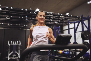 Fototapeta na wymiar Fit mature woman smiling while running on a treadmill