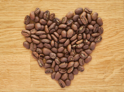 Black Coffee Beans Seed In Heart Shape On Brown Wooden Table, Dark Cofee Arabica Robusta Roasted Grain Flavor Aroma Cafe, Natural Coffe Shop Background, Top Close Up View From Above,