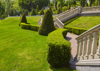 Stairs with stone railings balusters and iron lanterns on the background of the park with a luxurious landscape design walking path for walking