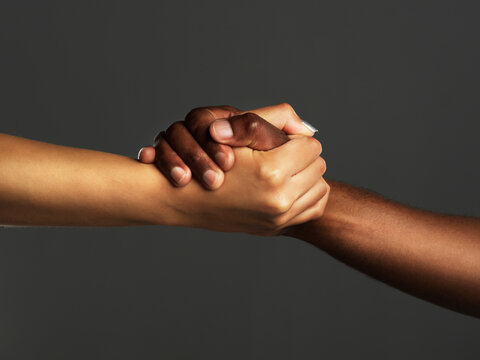 Everyone needs a helping hand. Studio shot of two unrecognizable people holding hands against a grey background.