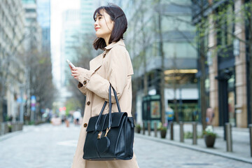 スマートフォンを手にビジネス街を歩く女性