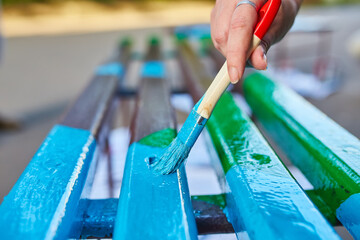 brush in hand paints a bench in bright colors, painting a garden bench