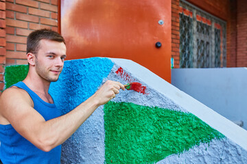 The guy paints the wall with a brush in bright colors