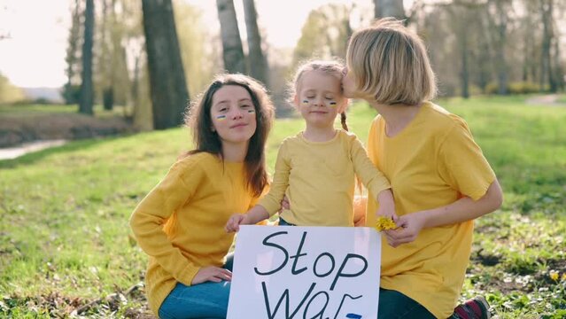 Ukrainian family calls to stop war. Mom with two daughters hold poster with inscription STOP WAR in their hands and look at camera.