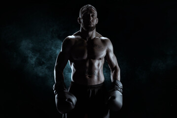 Kickboxer in black gloves posing on a background of smoke. The concept of mixed martial arts.
