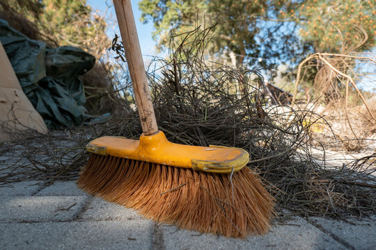 Pessoa a varrer o ch&atilde;o sujo com restos de giestas secas com uma vassoura