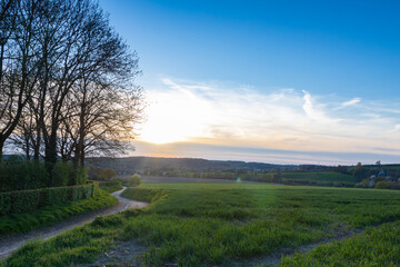 A spring landscape with rolling hills in the south of Limburg during a spectacular sunset with a dirt road which seems to lead to the sun