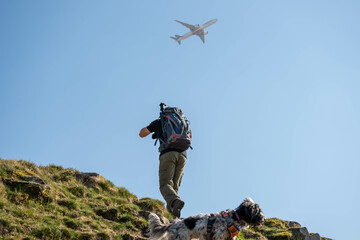 Fototapeta premium Man with camera equipment hiking while plane flies overhead - location scouting