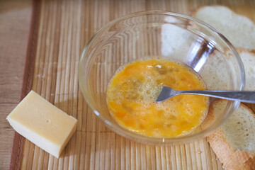 Close-up of mixed eggs in a clear glass bowl on the kitchen table with a piece of hard cheese. Step-by-step cooking of eggs for breakfast