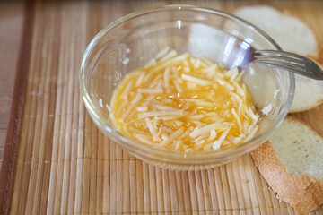 Close-up of mixed eggs in a transparent glass bowl with grated cheese. Step-by-step cooking of eggs for breakfast