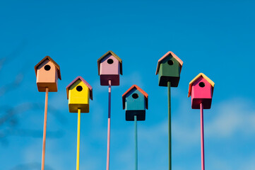 welcome to the spring garden birds to a group of colorful wooden birdhouses on a blue sky background