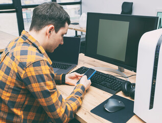 Man addicted to his phone surfing the social media on his phone while must works with his laptop