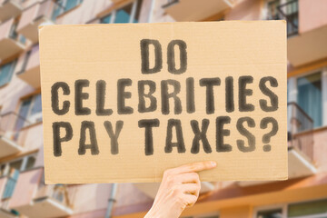 The question " Do celebrities pay taxes? " is on a banner in men's hands with blurred background. Savings. Spend. Status. Success. Tax. Treasure. Vip. Wealth. Majestic. Money. Place. Position. Report