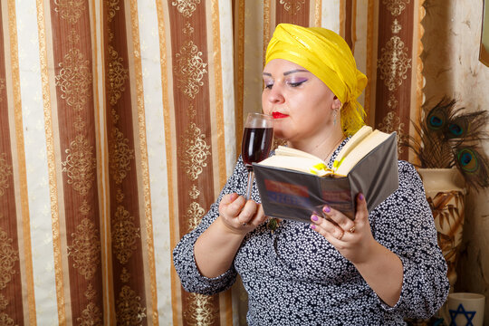A Jewish woman in a Kisui Rosh headdress drinks Avdala wine with a siddur in her hand.