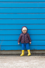 Young toddler wears blue pants standing next to blue matching siding on a building  silly side eye and expression © Julia Beatty