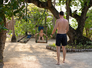 Father rocking his son on a rope swing in the jungle in the Maldives