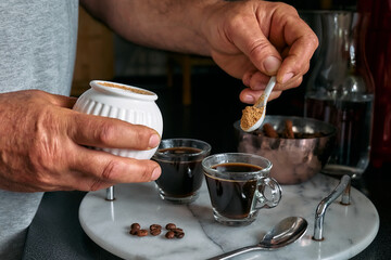 Man preparing classic Italian coffee in the mocha in the kitchen and pouring sugar into the coffee in small coffee cup. Coffee brake. Morning habit.