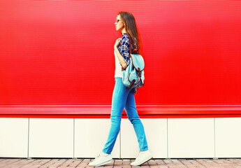 Obraz na płótnie Canvas young woman full-length wearing backpack walking in the city on red background, blank copy space