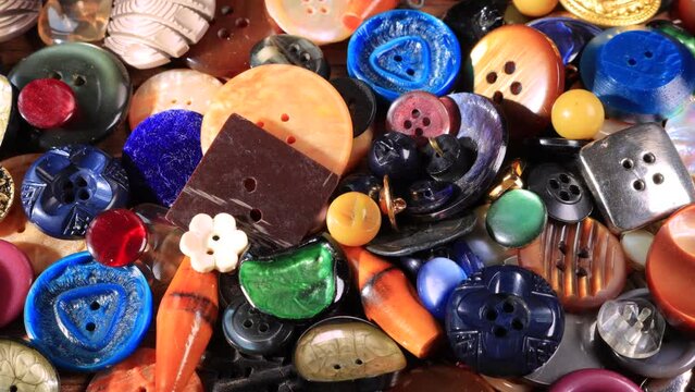 Slow pan to the right on set of vintage buttons on old wooden table. Old-fashioned colorful clothe buttons. Close-up moving slider shot of a pile of dress buttons
