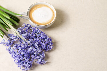 Obraz na płótnie Canvas Morning spring coffee in a cup of foam next to it lie blue hyacinths on a beige background