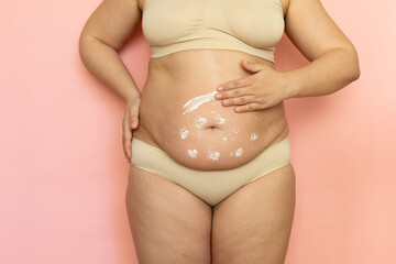 Cropped overweight woman in underwear applying moisturizer cream lotion to her abdomen. Fat removal. Wearing underwear, doing self massage to puffy skin. Cellulite obesity. Postnatal, body positive