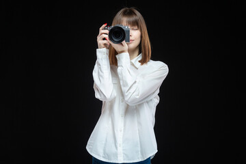 Portrait of a young woman wearing a white shirt holding a camera in her hand. The concept of a successful photographer. Isolated black background.