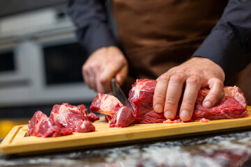 A butcher in an apron in the kitchen cuts pork on a wooden board. Steak.