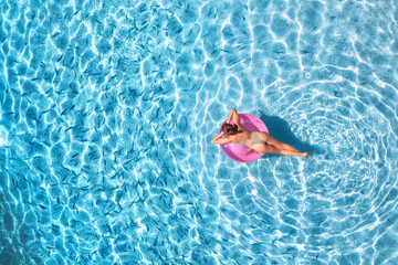 Aerial view of a young woman swimming with pink swim ring in blue sea with school of fish at sunset...