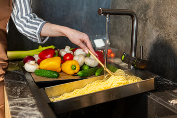 Close-up. A woman in an apron cooks spaghetti in the kitchen.