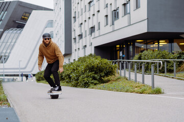Young man in a helmet rides an electric skateboard. Onewheel rider in an urban background. copy...
