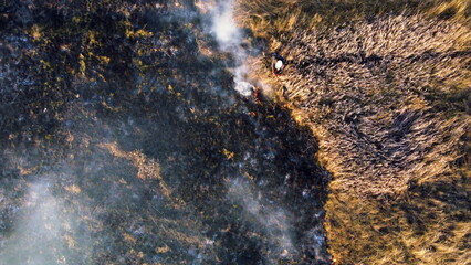 Aerial view Fire extinguishing. Fireman extinguishing burning dry grass. Open flames of fire and smoke. Yellow dry grass and black ash from burnt plants.Ecological catastrophy. Fire on field in steppe