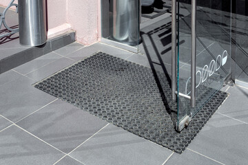 threshold made of gray ceramic stone tile at entrance to store with rubber foot mat and open glass...