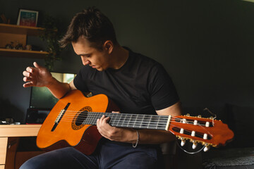 Obraz premium A young guy is playing a classical guitar in his room during the day